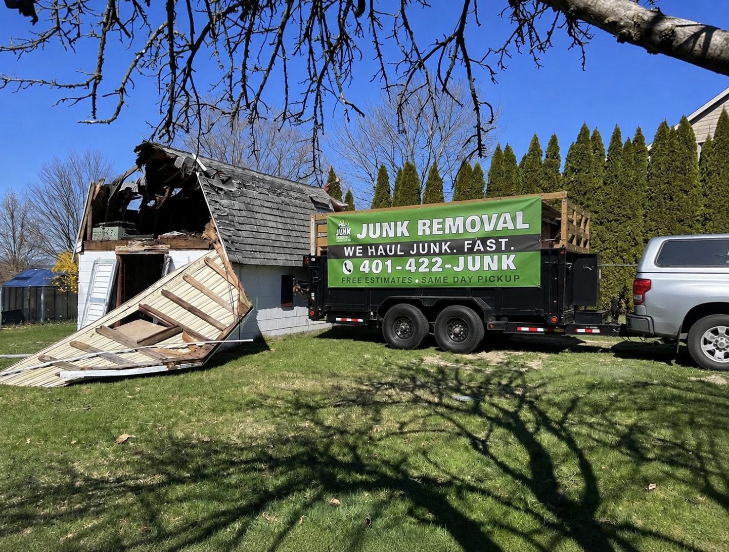 Shed mid-demolition with the loaded junk removal trailer parked beside it